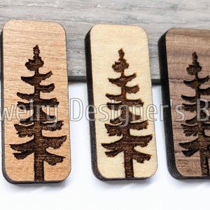 K&ouml;nnte beinhalten: Drei rechteckige Holzornamente mit einem lasergeschnittenen Design eines Kiefernbaums. Die Ornamente sind in drei verschiedenen Holzt&ouml;nen gehalten: hellbraun, beige und dunkelbraun.