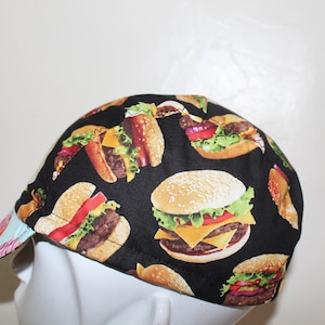 May include: A black cycling cap with a pattern of colorful hamburgers. The cap has a blue and pink brim.