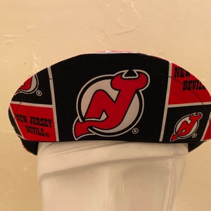 May include: A black and red fabric hat with a New Jersey Devils logo. The hat is made of a patchwork of different fabrics with the Devils logo repeated throughout.