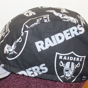 May include: Black and white cycling cap with the Raiders logo and text repeated throughout. The cap has a gray brim.