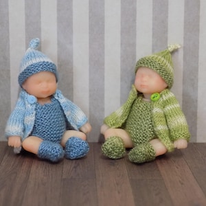May include: Two knitted baby dolls, one in blue and white and one in green and white, wearing matching hats and booties.