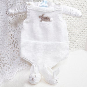 Op de afbeelding: Wit gebreide baby-romper met een bruine konijn geborduurd op de voorkant. De romper is mouwloos en wordt geleverd met bijpassende konijn-schoentjes.