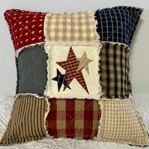 May include: A patchwork pillow with a frayed edge features a red, white, and blue star design. The pillow is made of various plaid and striped fabrics.