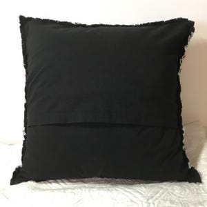 Peut inclure: Oreiller noir avec un motif patchwork blanc et color&eacute; sur le devant. L'oreiller a un bord effiloch&eacute; et est fait de tissu.