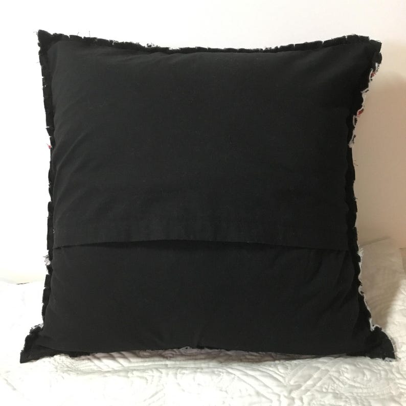 Peut inclure: Oreiller noir avec un motif patchwork blanc et color&eacute; sur le devant. L'oreiller a un bord effiloch&eacute; et est fait de tissu.