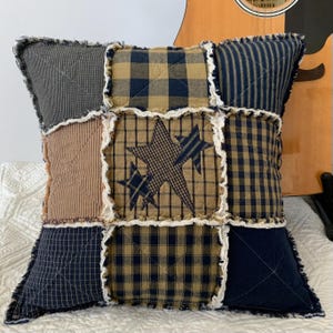 May include: A patchwork pillow with a blue and brown plaid design. The pillow has a frayed edge and features a star design in the center.