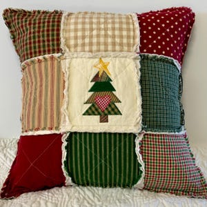 May include: A patchwork pillow with a Christmas tree design in the center. The pillow is made of various fabrics in red, green, white, and brown. The tree is green with a red heart and a yellow star.