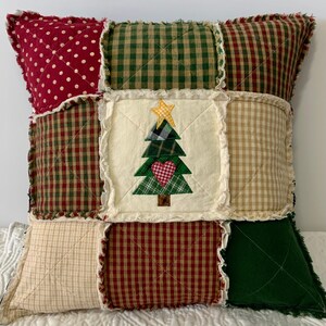 May include: A patchwork pillow with a Christmas tree design in the center. The pillow is made of various fabrics in red, green, and beige with a gingham pattern. The tree is green with a red heart and a yellow star.