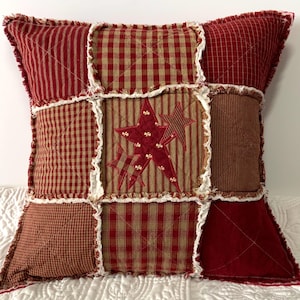 May include: Red and brown patchwork pillow with a star design in the center. The pillow has a frayed edge.