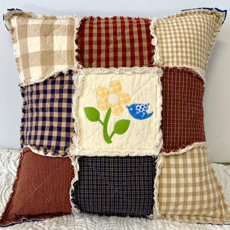 Peut inclure: Un coussin patchwork avec un fond cr&egrave;me et une vari&eacute;t&eacute; de tissus &agrave; carreaux en rouge, marron, bleu et beige. Le carr&eacute; central pr&eacute;sente une fleur jaune avec une tige verte et un oiseau bleu.