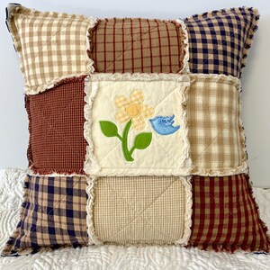 Peut inclure: Un coussin en patchwork avec un motif &agrave; carreaux cr&egrave;me, rouge et bleu. Le coussin pr&eacute;sente un motif brod&eacute; de fleurs et d'oiseaux au centre.