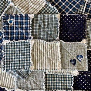 May include: A patchwork quilt featuring squares of various blue and white patterned fabrics, including gingham, polka dots, and stripes. Some squares have heart-shaped appliqués. The quilt has a frayed edge.