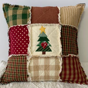 May include: A patchwork pillow with a Christmas tree design in the center. The pillow is made of various fabrics in shades of red, green, brown, and white. The tree is green with a yellow star on top and a red heart in the center.