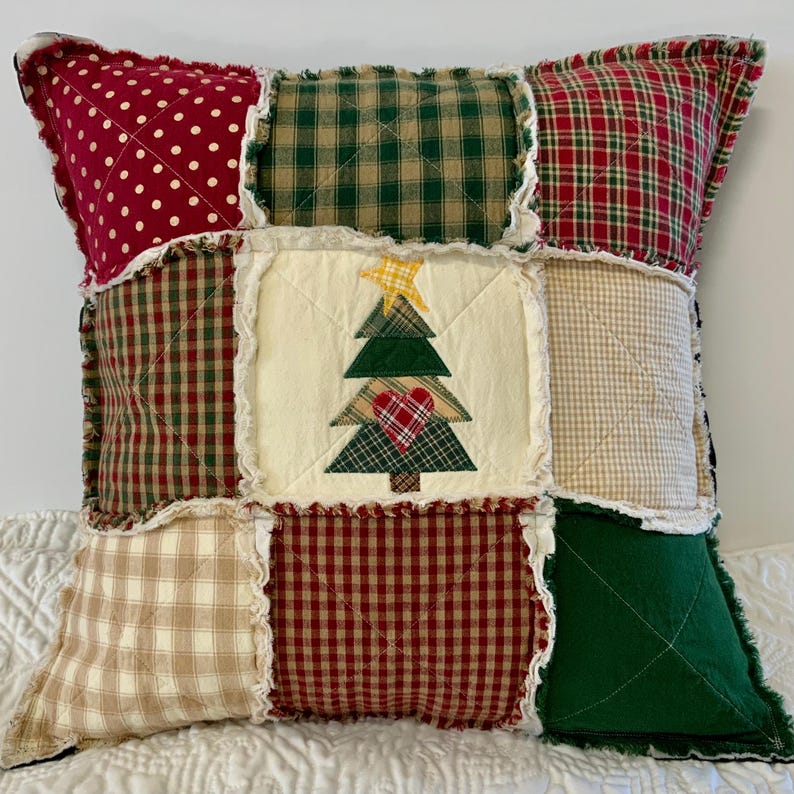 May include: A patchwork pillow with a Christmas tree design in the center. The pillow is made of various plaid and gingham fabrics in red, green, and tan.