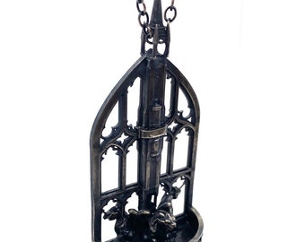 May include: A silver necklace with a detailed pendant featuring a gothic-style window with a spire and two gargoyles at the base.