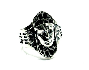 May include: A silver ring with a detailed design of a face. The face is surrounded by a geometric pattern.