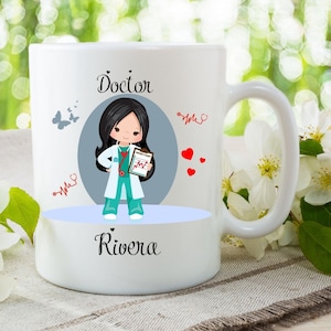 May include: White ceramic mug featuring a cartoon doctor with black hair, wearing a teal uniform and holding a patient chart. The mug has the word "Doctor" above the illustration and "Rivera" below. Red hearts and stethoscopes decorate the mug.