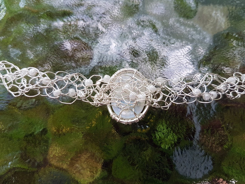 May include: A silver wire wrapped necklace with white beads and a white stone pendant.