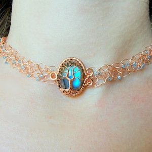 May include: A copper wire choker necklace with a blue labradorite gemstone pendant featuring a wire-wrapped tree design.