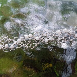 May include: A silver chain bracelet with white beads. The bracelet is made of wire and has a delicate, intricate design.