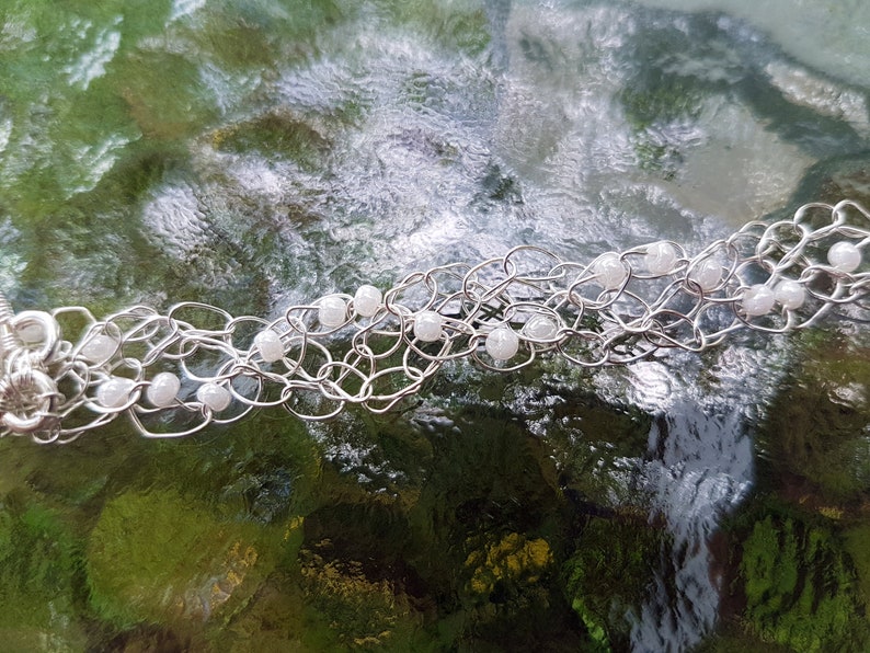 May include: A silver chain bracelet with white beads. The bracelet is made of wire and has a delicate, intricate design.