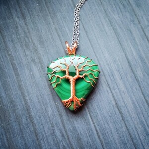 May include: A pendant necklace featuring a teardrop-shaped malachite stone with a copper wire tree design. The pendant hangs from a silver chain. The malachite stone is a vibrant green color.