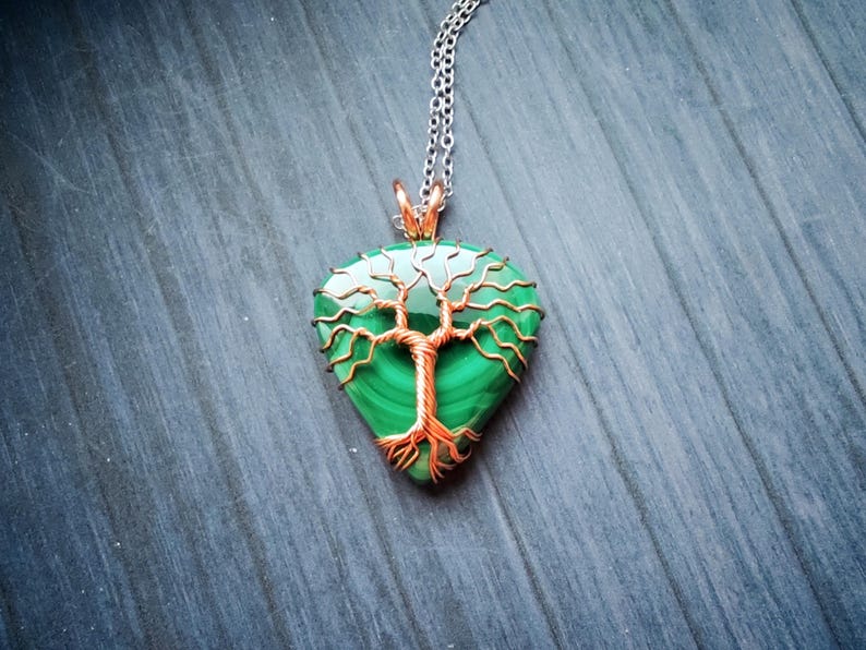 May include: A pendant necklace featuring a teardrop-shaped malachite stone with a copper wire tree design. The pendant hangs from a silver chain. The malachite stone is a vibrant green color.