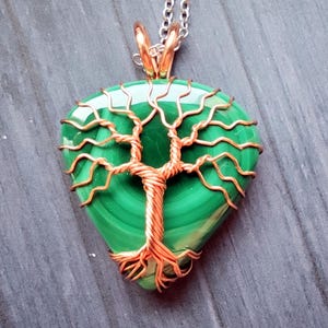 May include: A handcrafted pendant featuring a polished, teardrop-shaped malachite stone. The green stone is intricately wrapped with copper wire in a tree-of-life design, suspended from a silver chain. The pendant's dimensions are approximately 1.5 inches in length.