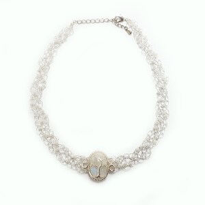 May include: A silver necklace with a delicate chain and a large oval pendant featuring a moonstone.