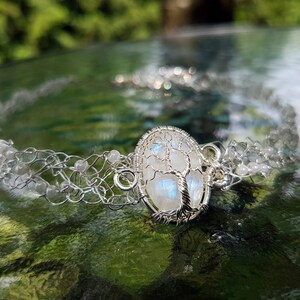 May include: A silver wire wrapped moonstone pendant with a tree of life design, set in a silver chain with white beads.