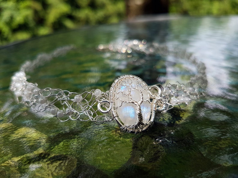 May include: A silver wire wrapped moonstone pendant with a tree of life design, set in a silver chain with white beads.
