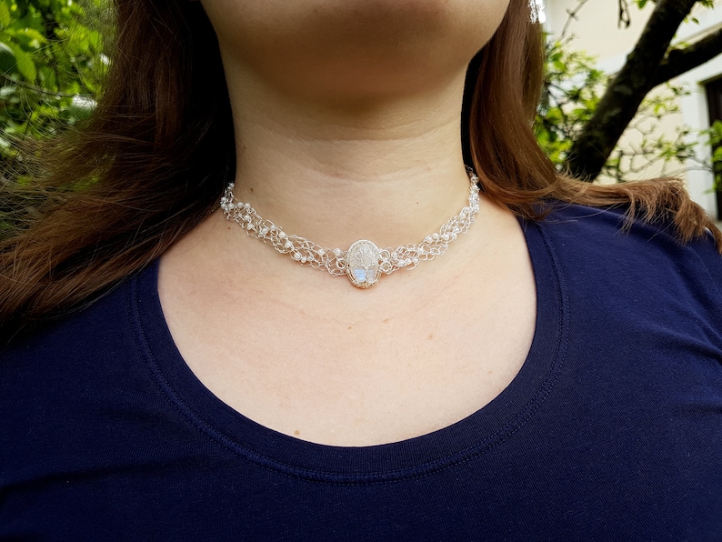 May include: A silver choker necklace with a white oval pendant. The necklace is made of small silver beads and wire.