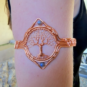 May include: A copper wire tree of life bracelet with a blue gemstone. The bracelet is designed in a diamond shape and has a woven wire design.