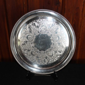May include: A silver serving tray with a decorative, embossed floral design. The tray has a raised rim and a beaded edge.
