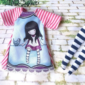 May include: A pink and white striped dress with a blue and white print of a girl and a bird. The dress has a white lace trim. A pair of white and blue striped leggings.