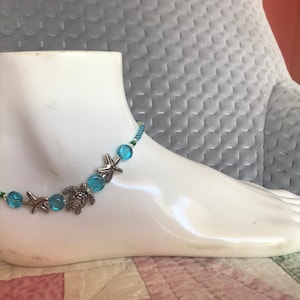 May include: A blue and silver anklet with a turtle and starfish charms. The anklet is made with small blue beads and silver beads.