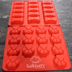May include: Red silicone baking mould with two sections. The top section has 18 bone-shaped cavities. The bottom section has 12 paw print-shaped cavities. The mould is labelled "Gastroworx Kitchen Gadgets by Elk"