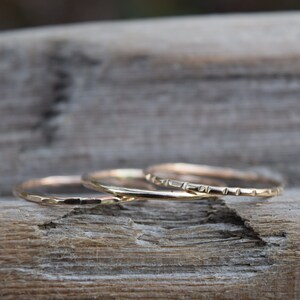 May include: Three thin gold stacking rings. The rings are smooth and have a hammered texture.