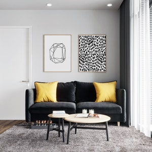 Puede incluir: Un sof&aacute; de terciopelo negro con dos cojines amarillos se encuentra en una sala de estar con una mesa de caf&eacute; de madera y dos mesas auxiliares m&aacute;s peque&ntilde;as. Dos impresiones enmarcadas en blanco y negro cuelgan de la pared detr&aacute;s del sof&aacute;.