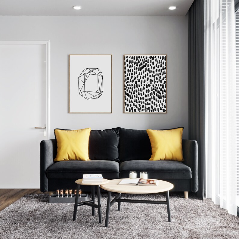 Puede incluir: Un sof&aacute; de terciopelo negro con dos cojines amarillos se encuentra en una sala de estar con una mesa de caf&eacute; de madera y dos mesas auxiliares m&aacute;s peque&ntilde;as. Dos impresiones enmarcadas en blanco y negro cuelgan de la pared detr&aacute;s del sof&aacute;.