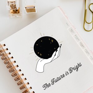 May include: A white spiral bound notebook with a black and gold illustration of a hand holding a crystal ball with stars. The text "The Future is Bright" is written in black cursive below the illustration.