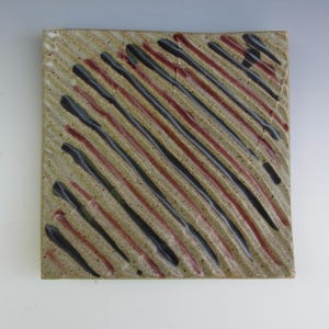 May include: Square ceramic plate with a textured surface. The plate features diagonal stripes in black and burgundy against a beige background. The design is hand-painted, giving it a unique, artistic look. This plate is suitable for serving food or as a decorative piece.