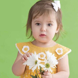 Pode incluir: Uma menina pequena vestindo um vestido amarelo com bolinhas brancas e uma gola de crochê com flores brancas. Ela está segurando um buquê de margaritas brancas.