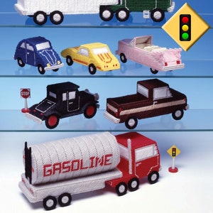May include: A collection of plastic model cars and trucks, including a semi-truck with a white trailer that says "Over-The-Road Trucking", a red and white petrol tanker truck, a black classic car, a brown pickup truck, a blue Volkswagen, a yellow sports car, and a pink convertible. There is also a red stop sign and a yellow traffic light.