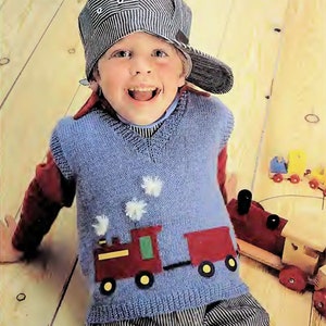 May include: A blue knitted vest with a train design on the front. The train is red, green, and yellow. The vest has a V-neck and is worn by a young boy wearing a striped baseball cap.
