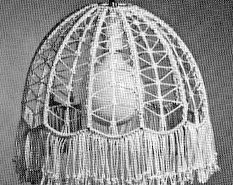 Puede incluir: Una pantalla de lámpara de crochet blanco con un borde de flecos. La pantalla tiene forma de cúpula y presenta un diseño delicado e intrincado.