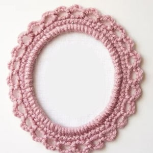 May include: A pink crocheted oval frame with a delicate lace pattern. The frame is perfect for adding a touch of handmade charm to your home decor.