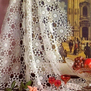 May include: White crocheted tablecloth with a delicate floral pattern, featuring a single pink rose and three red wine glasses on a wooden table.