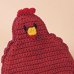 Puede incluir: Un portatoallas de cocina hecho a mano con forma de gallina de ganchillo rojo. La gallina tiene un pico amarillo, ojos negros y una cresta roja. El borde inferior está adornado con un borde amarillo con volantes. Accesorio de cocina.