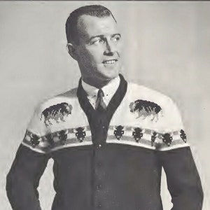Könnte beinhalten: Ein Schwarzweißfoto eines Mannes, der einen schwarz-weißen gemusterten Cardigan trägt. Der Pullover hat einen V-Ausschnitt und Knöpfe vorne. Der Mann lächelt und schaut nach rechts.